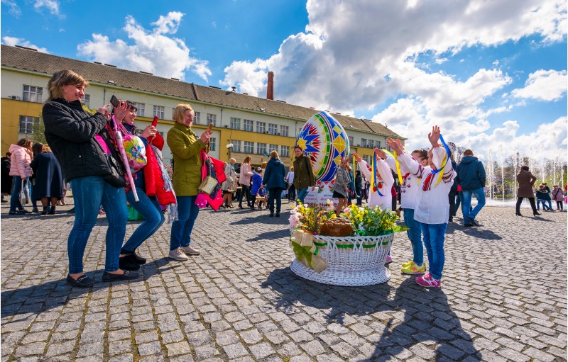 Uzhgorod, Ukraine - April 07, 2017: Celebrating Orthodox Easter in Uzhgorod on the Narodna square. women take photos of children near the big basket with flowers near huge egg on warm springtime day.