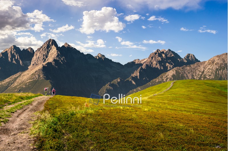 Composite Travel image. group of tourists in the distance go by the path through hillside to high mountains with rocky peaks