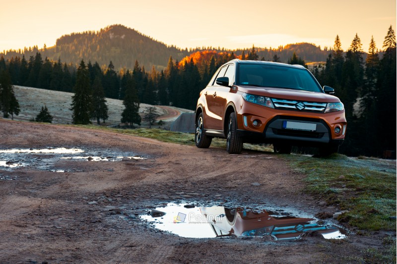 Apuseni, Romania - OCT 15, 2017: orange Suzuki Vitara SUV on a country road in mountains at sunrise. beautiful autumn landscape with spruce forest.travel Europe by car concept