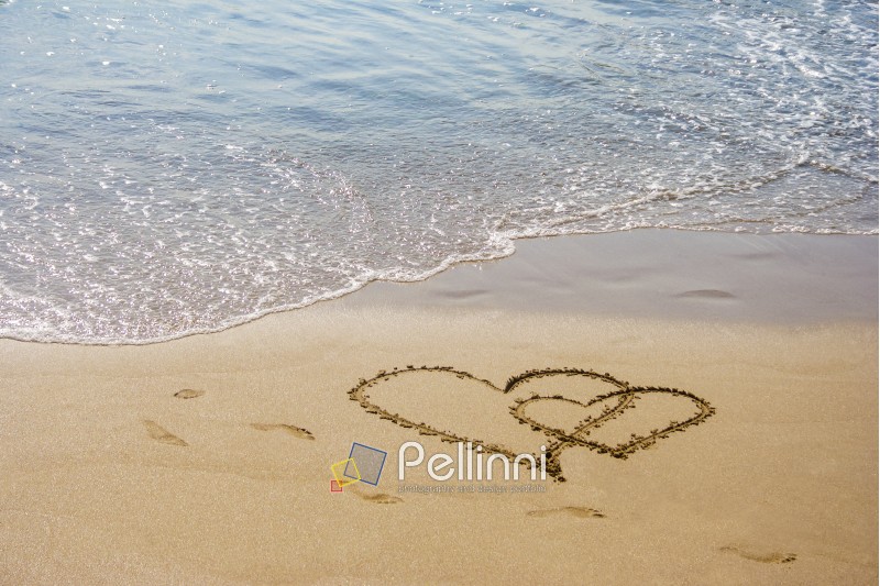 hearts couple drawn on the sand of a sea beach with few human steps oround them