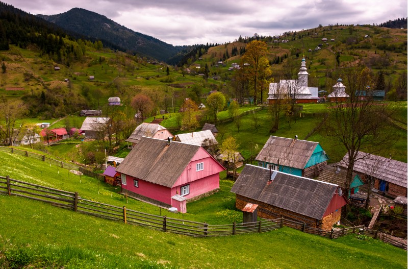 Synevyrs'ka Poliana village in Carpathians. lovely rural landscape with wooden fences on grassy slopes and a church on hillside among houses. beautiful nature springtime scenery in mountains