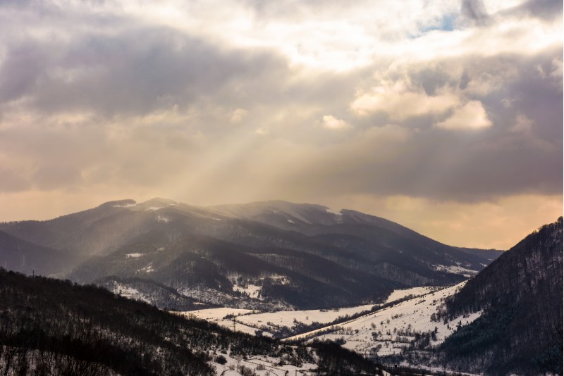 beam of light through cloudy sky over the mountain. lovely winter landscape