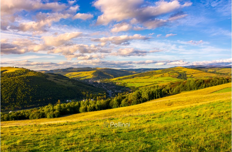 beautiful Carpathian countryside at sunset. village down in the valley in shade of a nearby mountain. beautiful colorful sky with clouds. Great water dividing ridge in the far distance