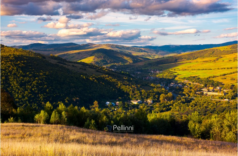 beautiful Carpathian countryside at sunset. village down in the valley in shade of a nearby mountain. beautiful colorful sky with clouds. Great water dividing ridge in the far distance