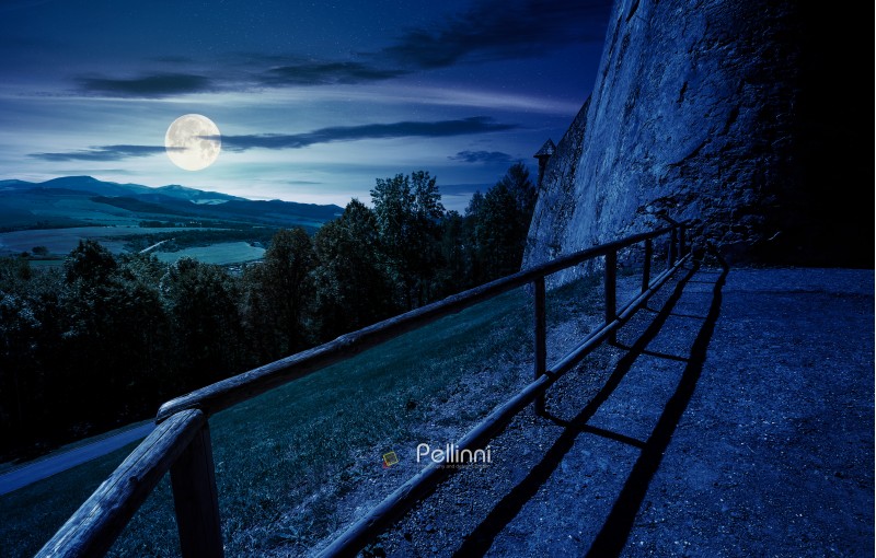 castle wall and railing on a hill at night in full moon light. view in to the beautiful mountainous landscape 