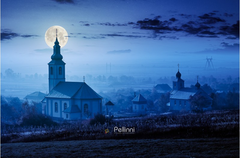 catholic and orthodox churches at foggy night in full moon light. lovely countryside scenery in autumn.
