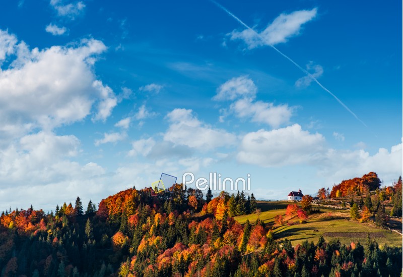 church on a hill under a beautiful cloudy sky. lovely autumn scenery with forest in red foliage