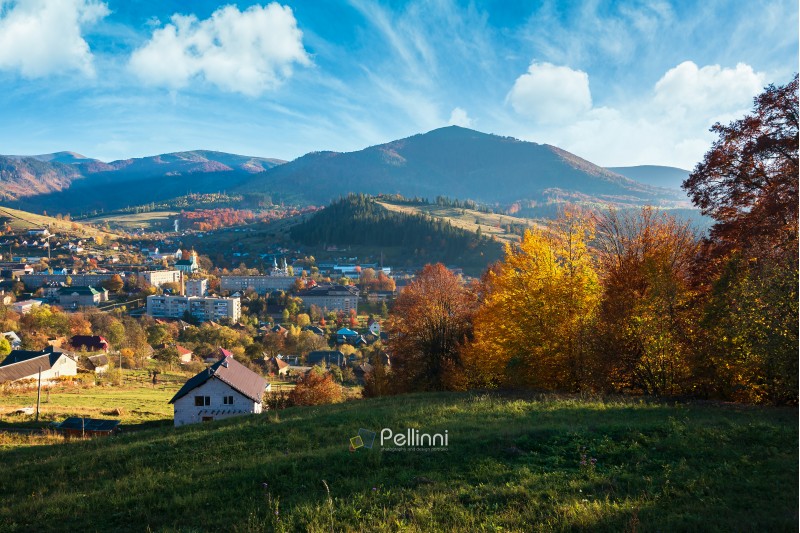 countryside beautiful autumn evening in mountains. small town in the distant valley. colorful trees on the hill. wonderful sunny weather with beautiful sky