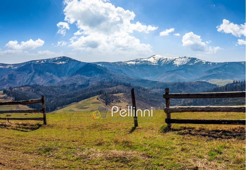 wooden fence on grassy hillside near mountains with snowy peaks in spring