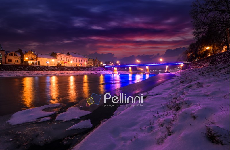 gorgeous evening cityscape of old european town Uzhgorod in winter. beautiful cloudy sky over the river Uzh with some ice and snow on the shore. citylights reflect on the water surface