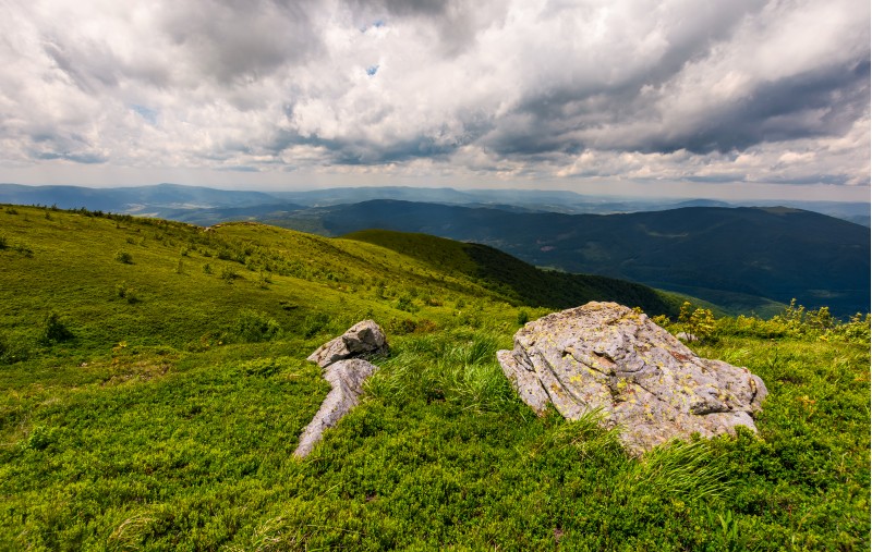 grassy slopes of Carpathian mountains. huge boulder on the edge of a hill side. mountain ridge under the cloudy sky in summer time