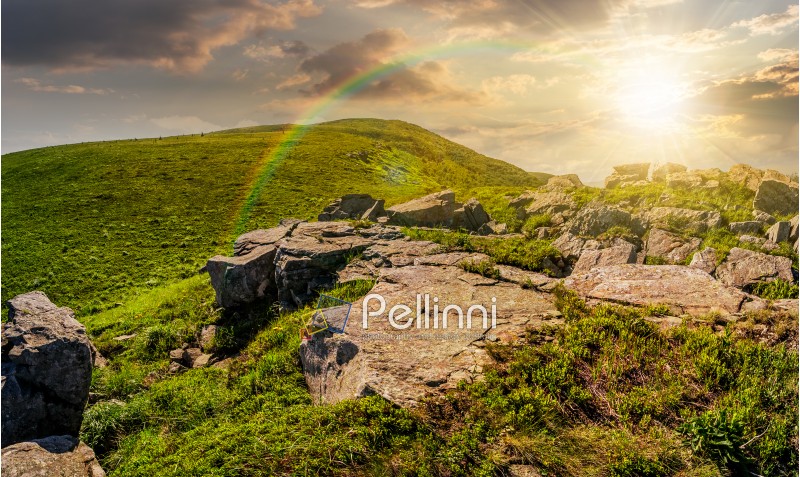 huge boulders on the edge of hillside at sunset. fine weather in summer mountain landscape with rainbow