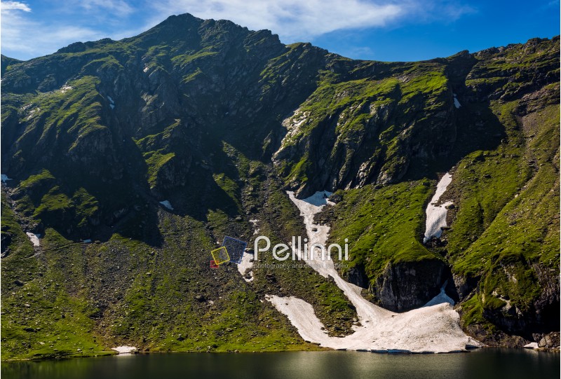 clear lake in mountains with snow and grass on rocky hillside. fine weather in picturesque summer scenery