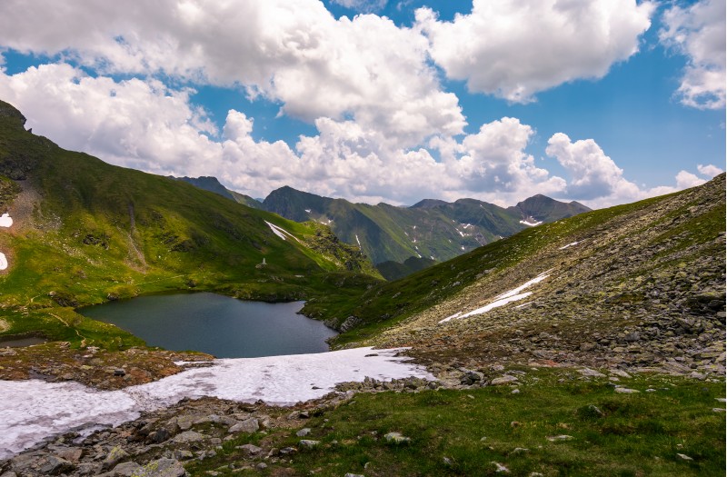 clear lake in mountains with snow and grass on rocky hillside. dramatic weather in picturesque summer scenery