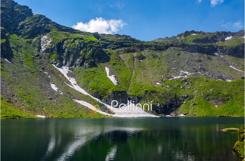 clear lake in mountains with snow and grass on rocky hillside. fine weather in picturesque summer scenery
