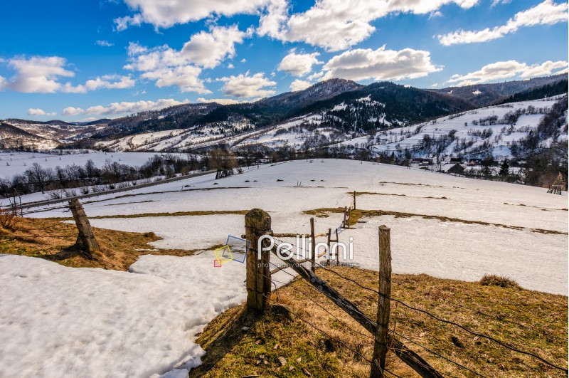 spring has come. last days of winter landscape. wooden fence on rural field with weathered yellow grass covered with snow. village at the foot of the mountain ridge