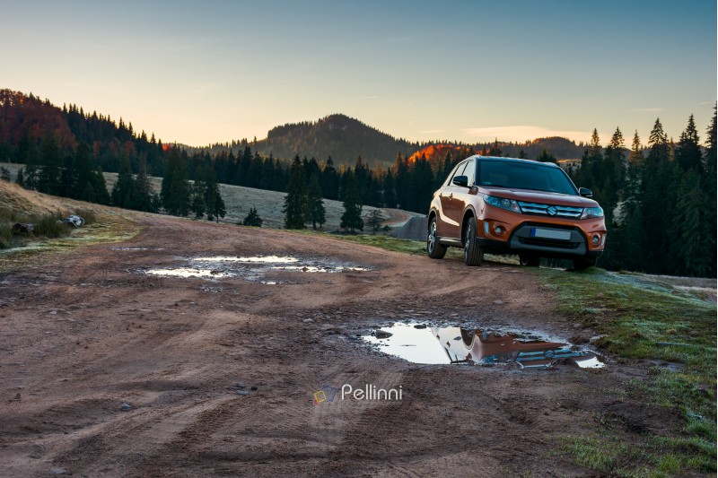 Apuseni, Romania - OCT 15, 2017: orange Suzuki Vitara SUV parked on the country road near forest in mountain at sunrise. beautiful autumn scenery. travel Europe by car concept