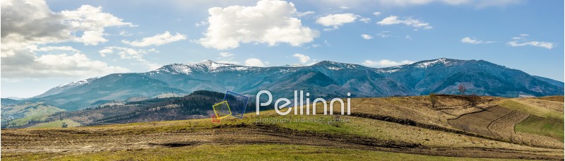Early spring highland landscape. Panorama of rural fields on hill side in mountains with snowy peaks