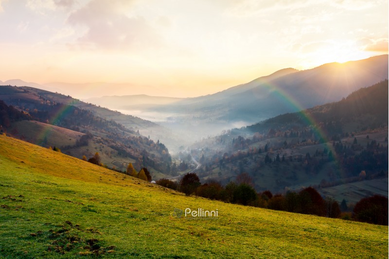 rainbow above the village in foggy valley. beautiful mountainous countryside at sunrise in autumn