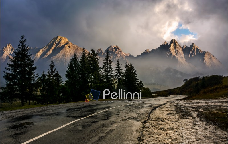 Travel destination concept image. Composite landscape of High Tatra mountain ridge. Curve asphalt road through spruce forest. Peaks lit by the sun in stormy weather with dramatic sky.