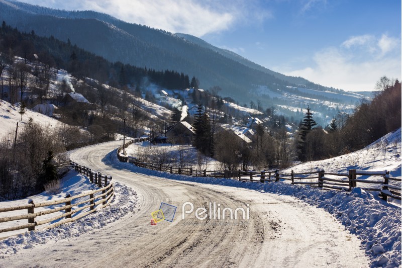 Empty asphalt mountain road through the village on bright winter day