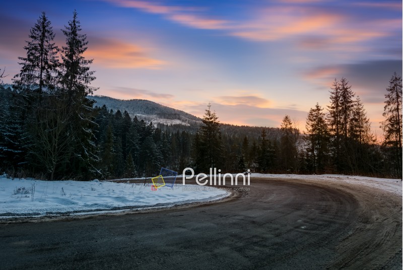 serpentine in winter mountains at sunset. gorgeous landscape with dark spruce forest on hillsides and red clouds on a blue evening sky. lovely transportation scenery of descend road turnaround
