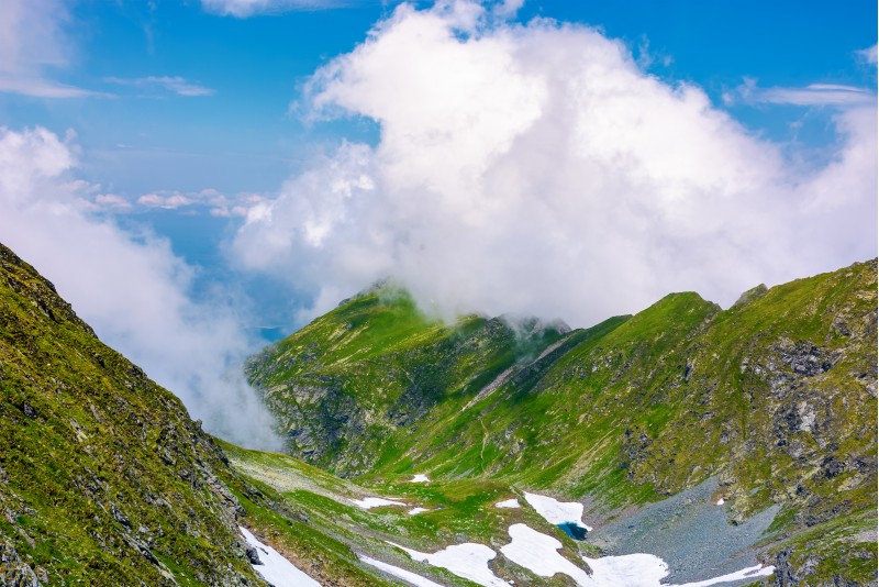 valley of Fagaras mountains in clouds. beautiful summer landscape with rocky cliffs and grassy slopes with spots of snow