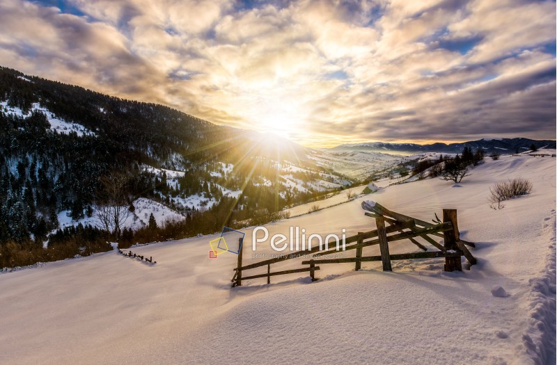 beautiful warm winter sunrise on cloudy morning in snow covered fields with wooden fence near rural area of Carpathian mountains
