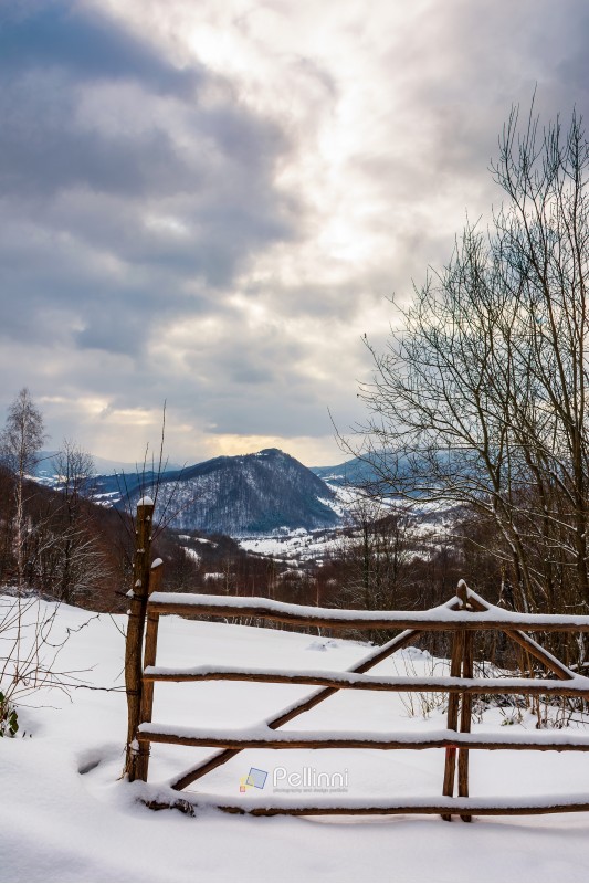 wooden fence on a snowy hill in mountains. gloomy winter weather