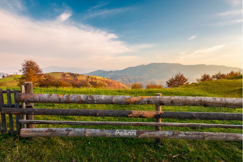 wooden fence on grassy rural field. distant mountain in morning haze. lovely autumn countryside
