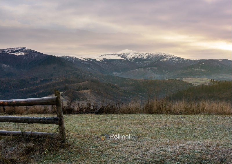 wooden fence on meadow with frozen grass. mysterious late autumn scenery with snow on tops of distant mountains
