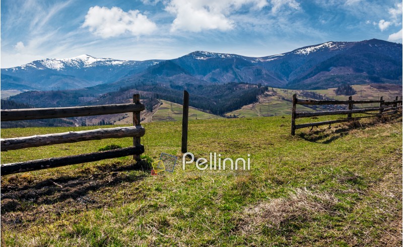 wooden fence on rural hill in spring. lovely mountainous landscape with snowy peaks in the distance