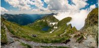 Gorgeous landscape of Fagaras mountains in summer. clouds rising above the rocky cliffs. lake Capra down the grassy slope in the valley. view from the tourist path on top of the ridge.