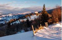 Synevyr, Ukraine - JAN 19, 2016: countryside in Carpathian mountains at sunrise. lovely scenery with wooden fence and coniferous forest on a snowy slopes. hotel and a village on hill in a distance