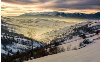 beautiful countryside in mountains at sunrise. village and rural fields on hillsides of valley covered with snow shine in morning light