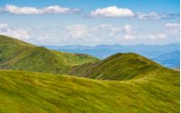 blue sky with some clouds over the green and grassy hills of Carpathian alps. road winds uphill the mountain meadow. beautiful minimalistic summer landscape in good day weather.