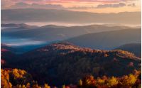 gorgeous red sunrise in mountains. forested hills in colorful fall foliage. fog in the distant valley