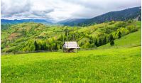 hay shed on a grassy field in mountains. beautiful countryside landscape in springtime. cloudy forenoon. village on the distant hills