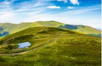 little pond on top of mountain ridge. gorgeous summer landscape with footpath through grassy hill and high clouds on a blue sky. wonderful tourism concept