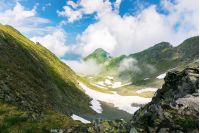 on the edge of rocky cliff of Fagaras valley. gorgeous landscape of Romanian mountains in rising clouds. popular travel destination. beautiful summer scenery with snow on the bottom of the valley