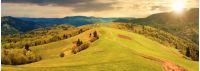 panorama of a countryside in mountains at sunset in evening light. path down the grassy rural hills rolling in to the distance. ridge beneath an overcast sky in spring