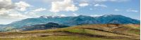 Early spring highland landscape. Panorama of rural fields on hill side in mountains with snowy peaks