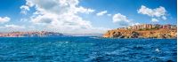 composite summer seascape. panoramic view of old resort town on a rocky cliff above the seashore. blue and calm water in the sea