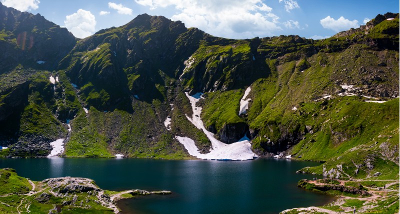 Belea lake in Fagarasan mountains of Romania. beautiful nature summer scenery with grassy slopes, rocky cliffs and some snow
