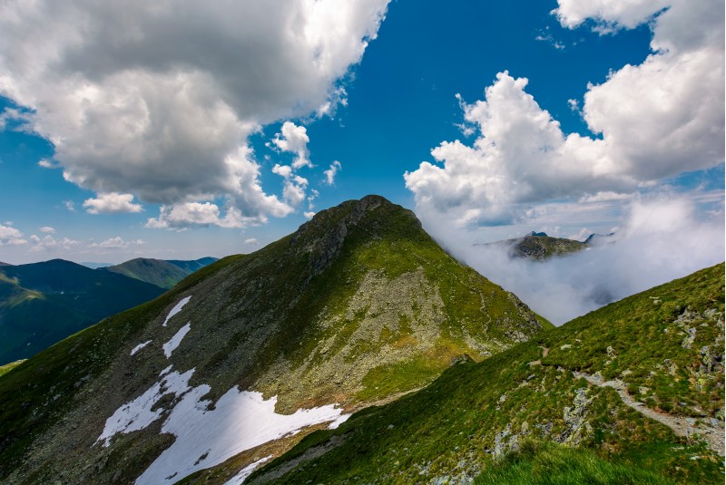 Peaks of mountain ridge among the clouds. Mighty formations with rocky tops and grassy hills. beautiful summer nature scenery on high altitude