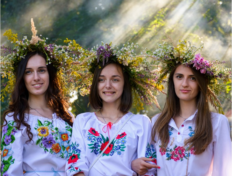 Uzhgorod, Ukraine - 07 Jul, 2016: Portraits of three Young ladies with traditional wreath on their heads. background of park with light coming through smoke. Popular holiday in Slavic culture