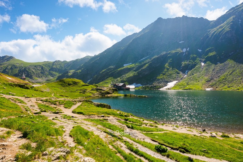 balea lake of romania. alpine landscape of fagaras mountains with pond. sunny weather with clouds on the blue sky above carpathians. snow and grass on the hillside in summer. calm water surface