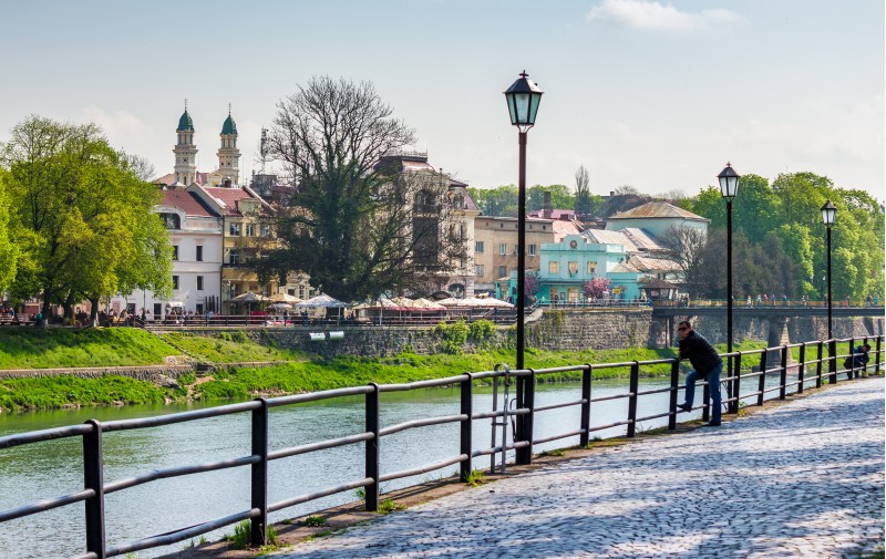 Uzhgorod, Ukraine - April 13, 2016: beautiful cityscape of the old central part of a town on the river Uzh in springtime, viewed from the Kyiv embankment with metal fence and lanterns