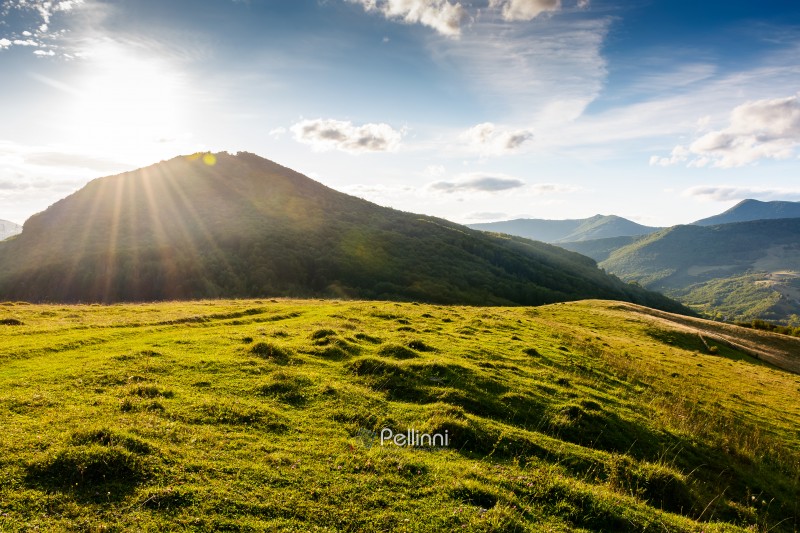 beautiful countryside at sunset. wonderful summertime landscape in mountains in evening light. scenic view of grassy field and rolling hills. rural scenery storytelling image under the rainbow