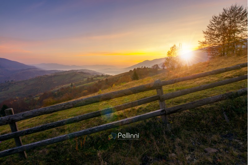 beautiful sunrise in mountains. countryside scenery in autumn. fence along the rural fields. distant mountains in haze